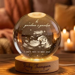 May include: A glowing crystal ball with a wooden base, featuring an ultrasound image and the text "hi grandma & grandpa" and "I can't wait to meet you!". The base is engraved with "Baby Thompson ARRIVING 2026".