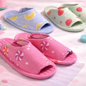 May include: A collection of colorful open-toe slippers. The slippers feature various patterns, including lemons, strawberries, and candy designs. The color palette includes pink, blue, and green, with a soft, inviting aesthetic. These slippers are ideal for indoor wear.