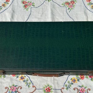 May include: A rectangular dark green storage case with a textured faux-alligator skin pattern. The case features a brown leather handle, two metallic latches on the front, and a circular logo in the top left corner with the text Chatteringsparrows.