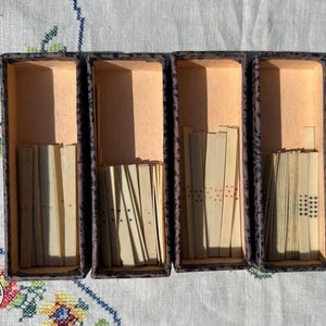 May include: Four rectangular boxes with dark speckled exteriors and light interiors, each containing a collection of thin, off-white rectangular game tiles. The tiles feature varying patterns of small black and red dots arranged in vertical rows.