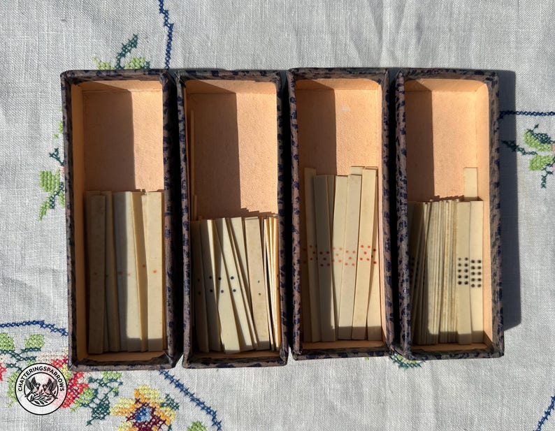 May include: Four rectangular boxes with dark speckled exteriors and light interiors, each containing a collection of thin, off-white rectangular game tiles. The tiles feature varying patterns of small black and red dots arranged in vertical rows.