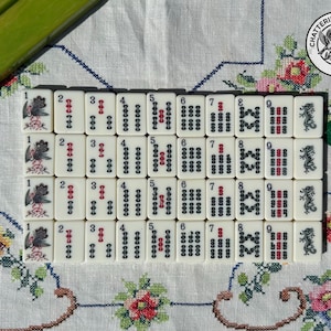 May include: A set of off-white Mahjong tiles arranged in four rows, featuring black and red ink designs including numbers one through nine, bird illustrations, and dragon symbols. A circular logo with two birds and the text CHATTERINGSPARROWS is visible.