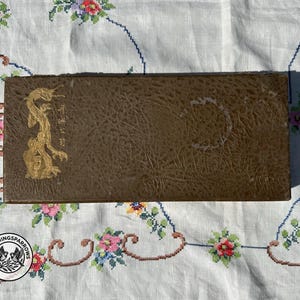 May include: A rectangular brown box with a textured surface featuring a gold-coloured dragon illustration on the left side. The box includes vertical gold-coloured Japanese characters next to the dragon and a circular mark on the right side.