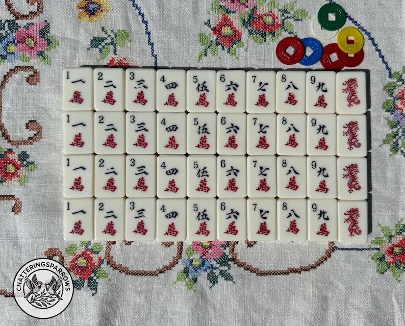 May include: A set of white Mahjong tiles arranged in four rows, featuring black numbers one through nine, red Chinese characters, and red dragon symbols. Five small, round, colored plastic counting tokens are placed in the upper right corner.