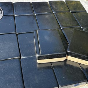 May include: A collection of rectangular mahjong tiles with glossy black faces and light-coloured wooden bases. The tiles are arranged in a grid pattern. A circular logo featuring two birds and the text CHATTERINGSPARROWS is visible in the top left corner.