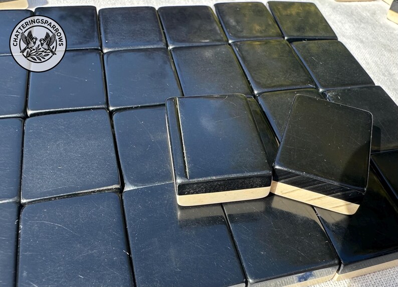 May include: A collection of rectangular mahjong tiles with glossy black faces and light-coloured wooden bases. The tiles are arranged in a grid pattern. A circular logo featuring two birds and the text CHATTERINGSPARROWS is visible in the top left corner.