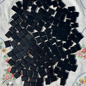 May include: A large collection of rectangular black tiles arranged in a scattered pattern. Each tile has a smooth, solid black surface with no visible markings or designs. The tiles are uniform in shape and size, creating a stark contrast.