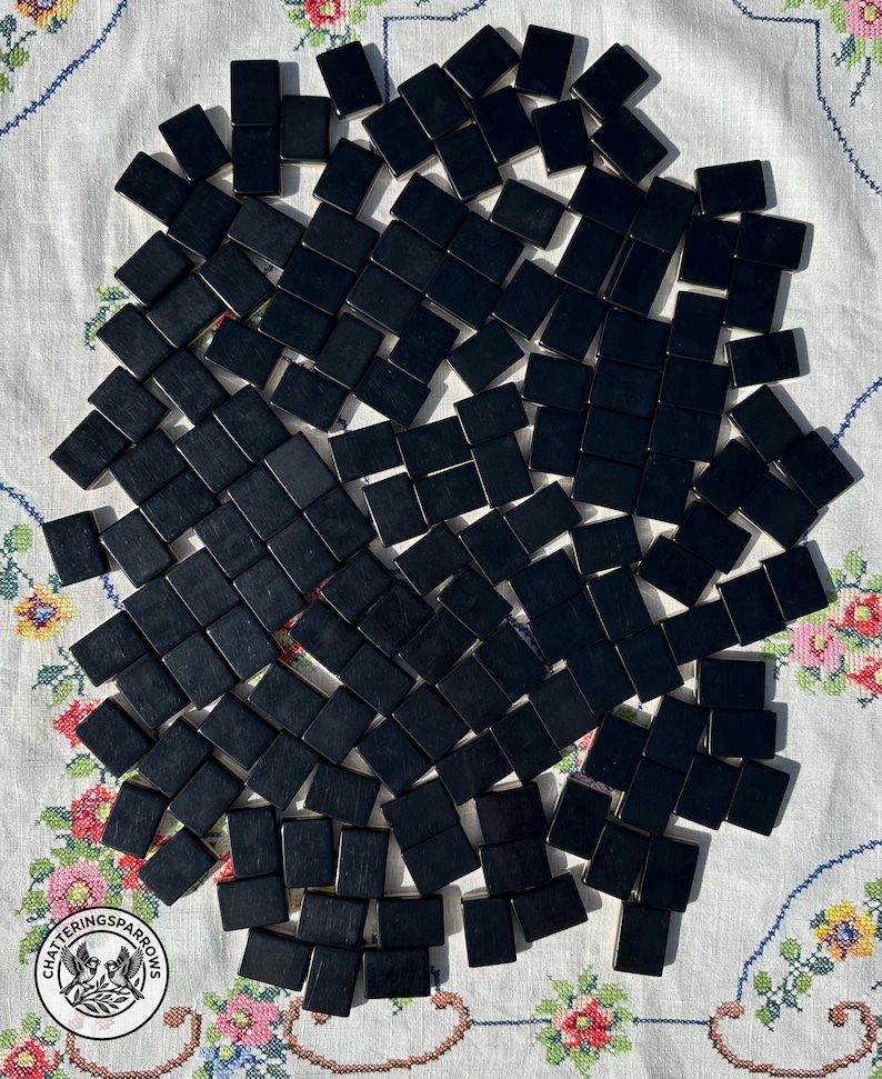 May include: A large collection of rectangular black tiles arranged in a scattered pattern. Each tile has a smooth, solid black surface with no visible markings or designs. The tiles are uniform in shape and size, creating a stark contrast.