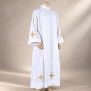 May include: A white liturgical alb featuring a high collar and long sleeves. The garment is decorated with gold-colored embroidered cross motifs positioned on the lower sleeves and near the bottom hem. The fabric is smooth and opaque.