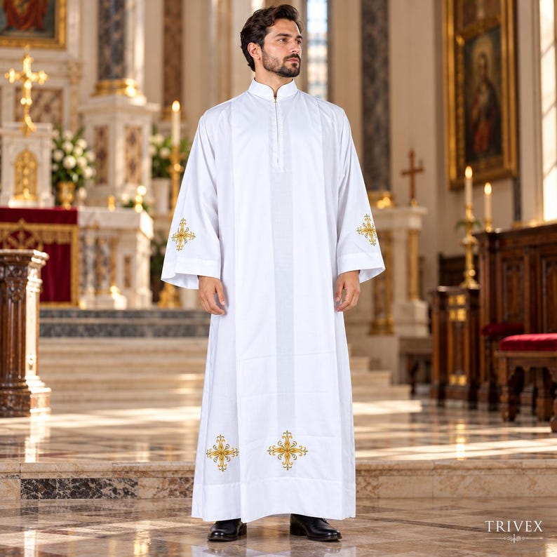 May include: A white liturgical alb featuring a high collar, long sleeves, and gold embroidered cross motifs on the cuffs and lower hem. The garment has a central vertical panel design and is worn with black dress shoes in a church setting.