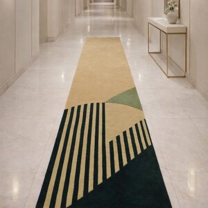 May include: A hallway runner rug with a geometric pattern. The rug has a beige base with dark green, olive green, and black vertical stripes. The hallway has white walls and marble flooring. The rug's design is modern.