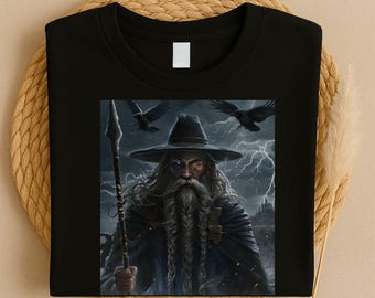 May include: Black t-shirt featuring a detailed illustration of a wizard with a long white beard, holding a staff, and wearing a hat. Two black ravens fly in the background, with a stormy sky and castle visible.
