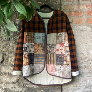 May include: A patchwork jacket with a brown and black plaid pattern on the sleeves and a variety of patterned fabric squares on the front. The jacket has a cream-colored lining and a brown trim. It hangs on a black hanger against a brick wall.