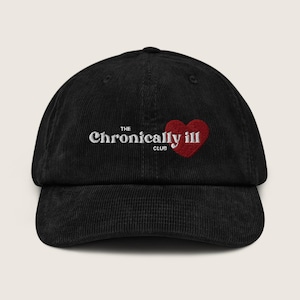 Op de afbeelding: Zwarte corduroy baseballcap met de tekst "The Chronically Ill Club" in witte letters en een rode hartafbeelding. De cap heeft een gebogen klep en een gestructureerde kroon, geschikt voor casual wear.