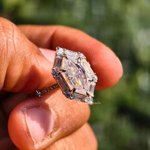 An image of the NovaLux Jewels Dutch marquise ring held up to demonstrate scale and its unique, slenderizing effect on the hand. The geometric stone creates a sophisticated focal point, while the dainty pave band adds to the modern minimalist aesthetic. Shimmering light reflections suggest a high-value anniversary or wedding gift that combines timeless elegance with contemporary design.
