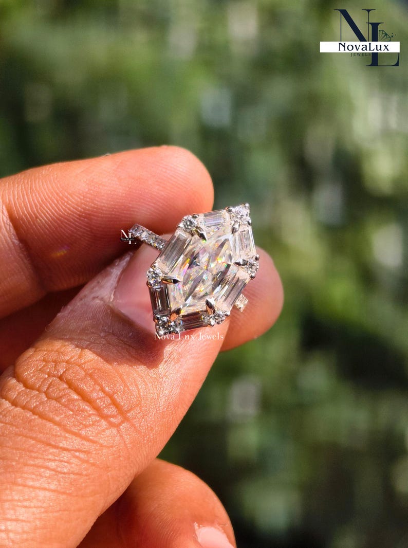 A breathtaking close-up of a NovaLux Jewels Dutch marquise-cut moissanite engagement ring held against a soft-focus nature background. The unique hexagon-modified marquise stone displays intense rainbow fire, flawlessly framed by a high-polish 14k white gold setting and a shimmering half-eternity pave band. This image highlights the "Architectural Luxury" aesthetic and high-end handcrafted quality of this modern bridal piec