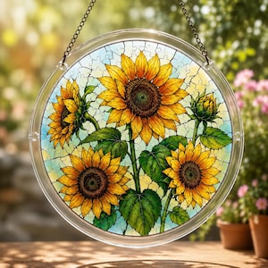 Può includere: Suncatcher rotondo in vetro trasparente con un design di girasoli. L'opera d'arte presenta diversi girasoli con petali gialli e foglie verdi. Lo sfondo è un mosaico di pezzi di puzzle azzurri e gialli. Con una catena per appenderlo.