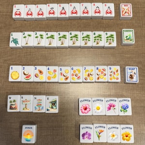 May include: A set of white rectangular mahjong tiles arranged in rows. The tiles feature colorful illustrations of crabs, palm trees, tropical fruits, flowers, beach scenes, and a joker tile. Each tile displays a number or text label.