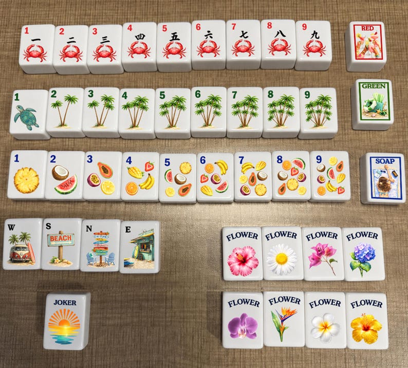 May include: A set of white rectangular mahjong tiles featuring colorful illustrations of crabs, palm trees, tropical fruits, beach scenes, and various flowers. Each tile displays a number or label, including Red, Green, Soap, W, S, N, E, Joker, and Flower.