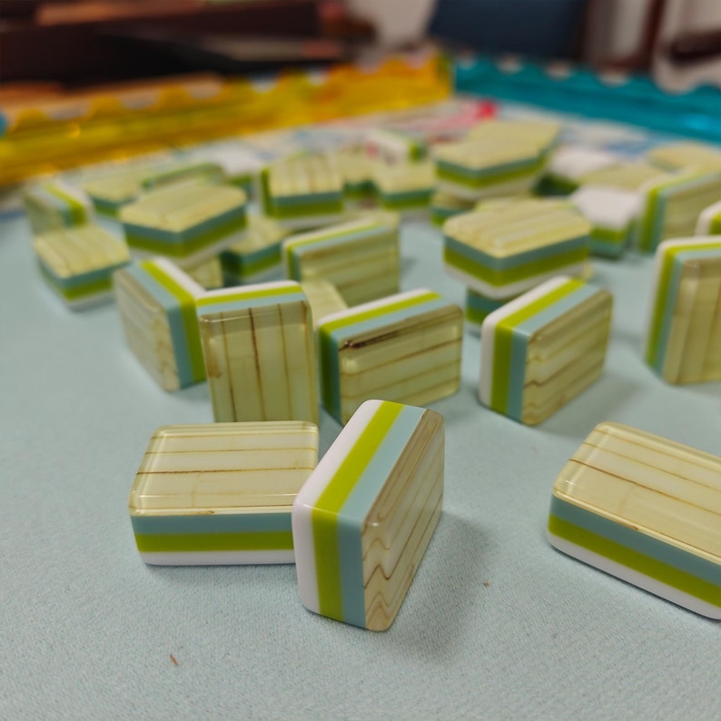 May include: A collection of rectangular mahjong tiles featuring a layered design with a translucent pale green top section, a solid lime green middle stripe, a light blue stripe, and a white base. The tiles have a smooth, glossy finish.