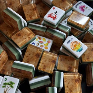 May include: A collection of mahjong tiles featuring a mix of designs, including a red crab with the number 9, a colorful fruit assortment, a sunburst graphic labeled JOKER, palm trees with the number 5, and a flower illustration with the text FLOWER.