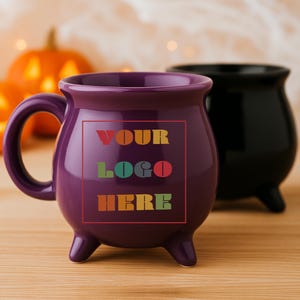 Puede incluir: Una taza morada con forma de caldero con asa y tres patas pequeñas. La taza tiene el texto "YOUR LOGO HERE" en un diseño colorido. Una taza de caldero negro está en el fondo. Las tazas están sobre una superficie de madera.