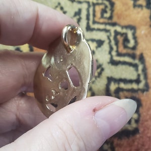 May include: Gold-toned metal pendant with a detailed cutout design. The pendant has a loop at the top for attaching to a chain.