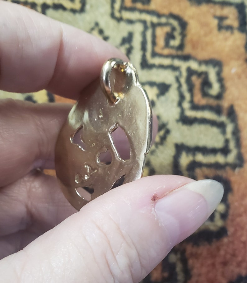 May include: Gold-toned metal pendant with a detailed cutout design. The pendant has a loop at the top for attaching to a chain.