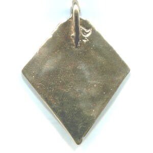 Puede incluir: Un colgante de color dorado en forma de diamante con un bucle en la parte superior para colgar. El colgante es liso y tiene una superficie ligeramente texturizada.