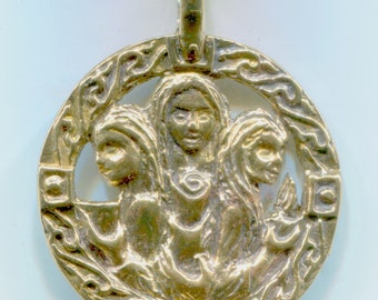 May include: A circular gold-toned metal pendant featuring a relief design of three figures arranged in a group. The figures are surrounded by an intricate, openwork border with swirling patterns and small square accents. A bail is attached at the top.