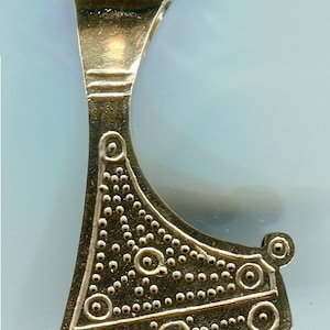 May include: A gold-colored metal axe pendant with a decorative design of circles and dots. The pendant has a loop at the top for hanging.