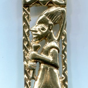 May include: Gold pendant with a detailed design of a person kneeling inside a Celtic knot frame.