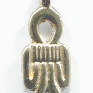 Peut inclure: Un pendentif en argent en forme de silhouette humaine stylisée avec une boucle en haut. La silhouette a une tête ronde avec un trou au centre, un corps côtelé et deux jambes.