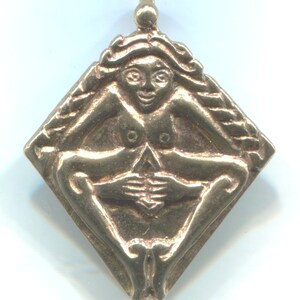 Puede incluir: Un colgante de oro en forma de diamante con una figura femenina en posici&oacute;n sentada. La figura est&aacute; desnuda y tiene las manos juntas frente a ella.