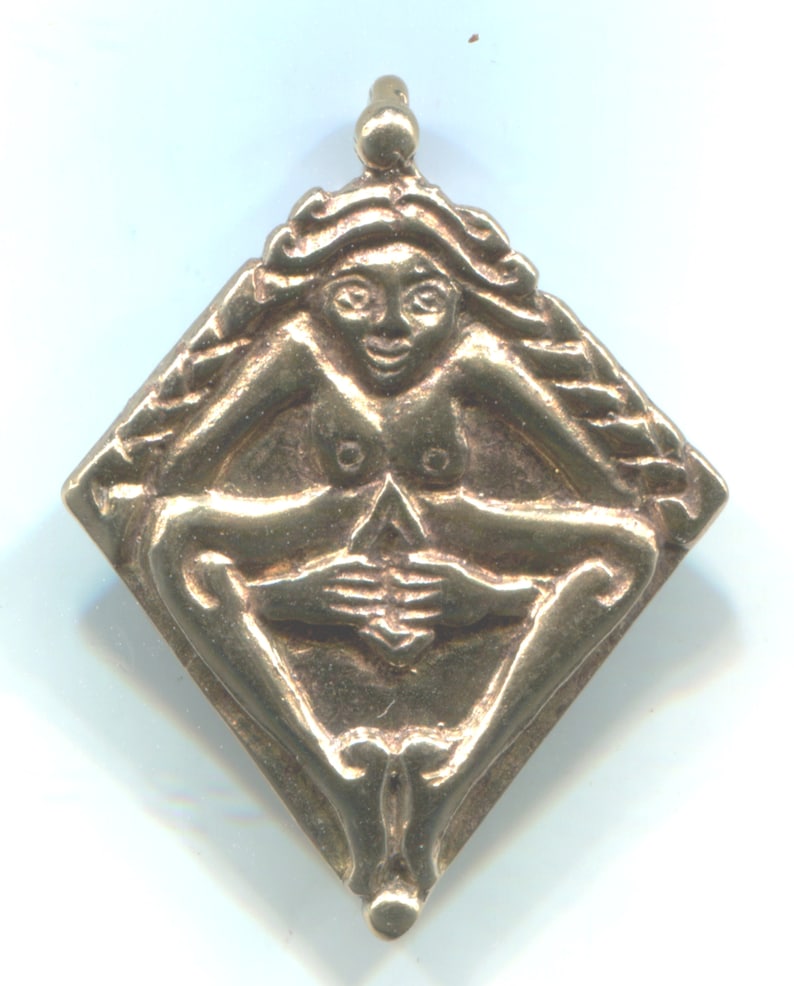 Puede incluir: Un colgante de oro en forma de diamante con una figura femenina en posici&oacute;n sentada. La figura est&aacute; desnuda y tiene las manos juntas frente a ella.