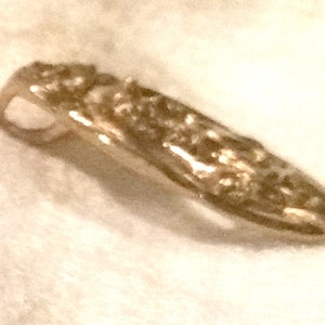 May include: A gold-toned pendant with a detailed design. The pendant has a loop at the top for attaching to a chain.