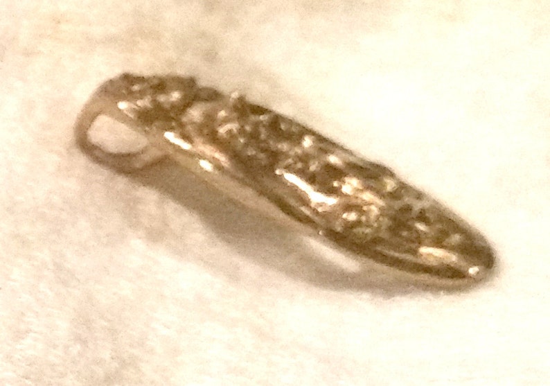 May include: A gold-toned pendant with a detailed design. The pendant has a loop at the top for attaching to a chain.