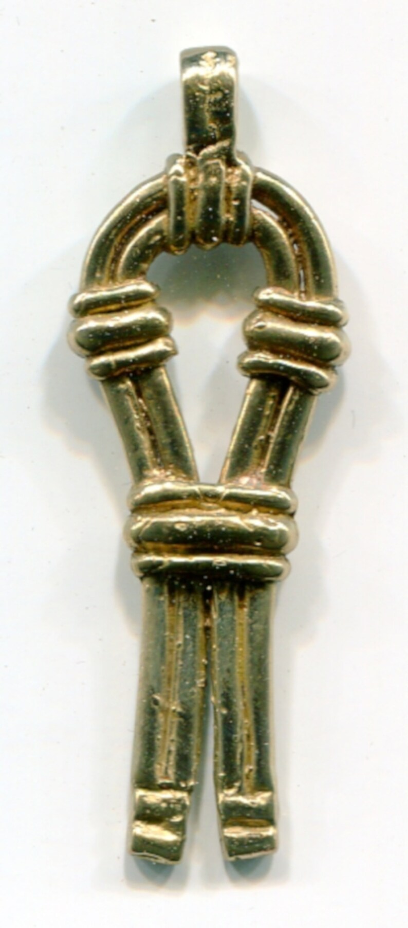 May include: A gold-colored pendant with a unique design. The pendant features a looped top, a central knot-like element, and two parallel, elongated sections. The overall shape is symmetrical and the surface has a textured appearance.