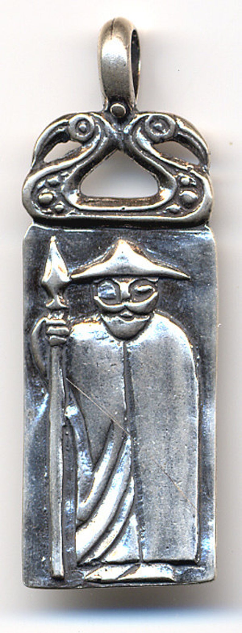 May include: A silver pendant featuring a stylized figure of a man wearing a hat and holding a spear. The pendant has a decorative top with a Celtic knot design.