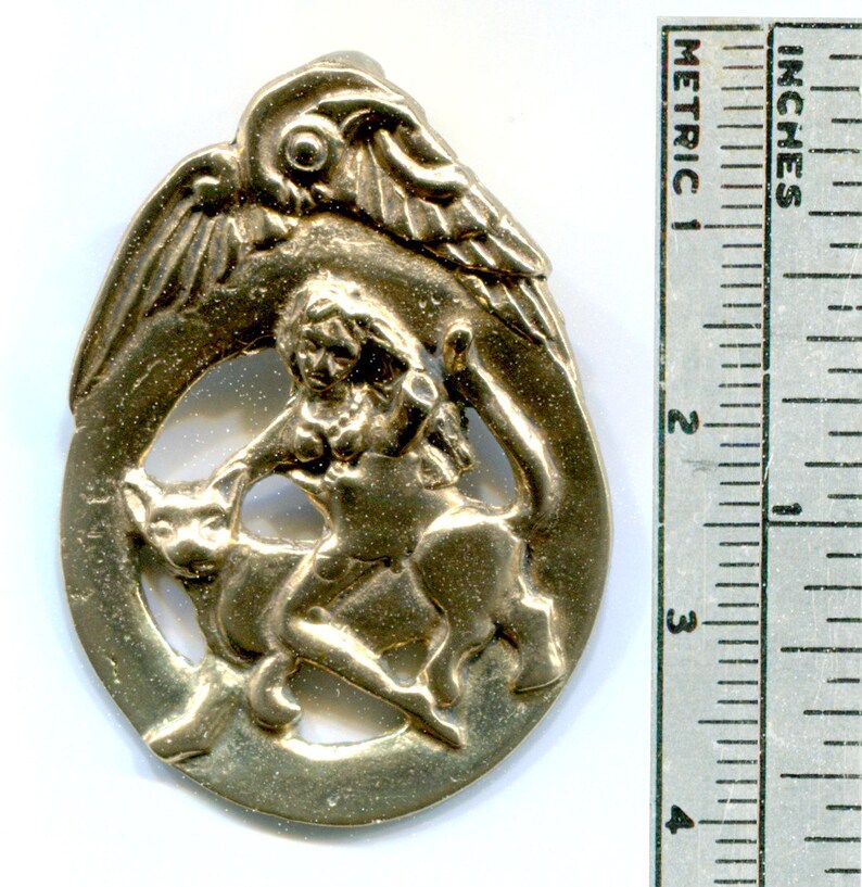 May include: A gold-toned metal pendant featuring a winged figure riding a mythical creature. The pendant is circular and has a detailed design.