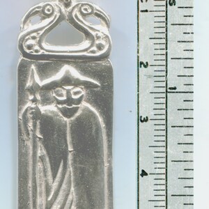 May include: Silver pendant depicting a figure in a hooded cloak holding a spear. The pendant is approximately 2 inches tall and has a detailed design.