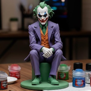 May include: A figurine of the Joker, seated on a green base, wearing a purple suit, orange vest, and green shirt. Paint pots and brushes surround the figure, suggesting a hobby or craft project. The Joker's face is painted with white, red, and blue makeup.