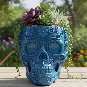 May include: A blue skull-shaped planter with intricate floral designs, filled with a variety of succulents. The planter is sitting on a wooden surface, with a copper watering can in the background. The succulents include a deep purple, green, and trailing plants.
