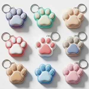 Può includere: Nove portachiavi a forma di zampa in vari colori, tra cui viola, verde, pesca, rosso, rosa e blu. Ogni portachiavi ha un anello argentato e un centro a contrasto. Disposti su sfondo bianco.