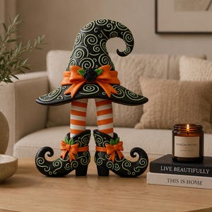 May include: A decorative figurine featuring a black witch hat with green swirl patterns and an orange bow, perched atop two legs with orange and white striped stockings and black curled-toe boots adorned with orange bows and green leaf accents.