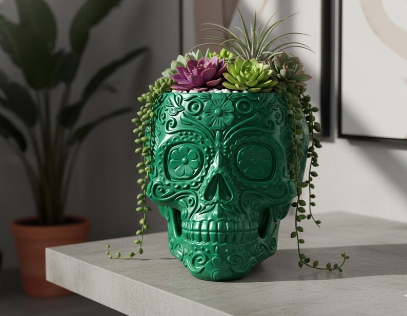 Pu&ograve; includere: Un vaso a forma di teschio verde con intricati disegni floreali. Il vaso &egrave; riempito con una variet&agrave; di piante grasse, tra cui una succulenta viola e verde pendente. Il vaso &egrave; realizzato in materiale lucido e poggia su una superficie grigia.