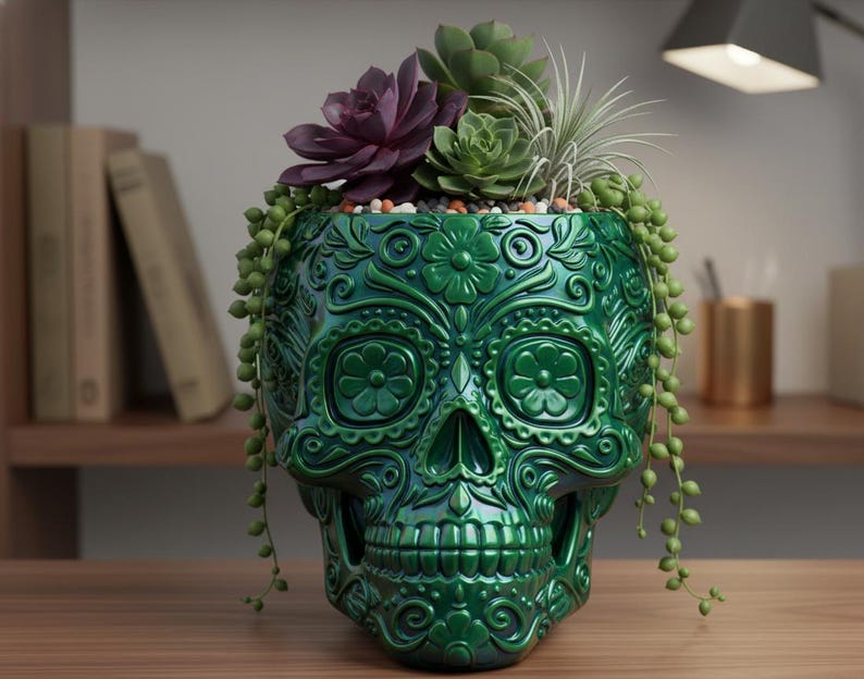 Pu&ograve; includere: Un vaso verde a forma di teschio con intricati disegni floreali, riempito con piante grasse e piante ricadenti. Il vaso lucido &egrave; posto su una superficie di legno, creando un elemento decorativo unico.