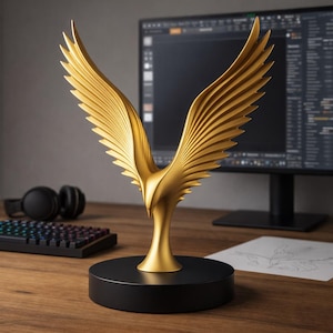 May include: A gold eagle sculpture with open wings, set on a black circular base. The sculpture features detailed, layered feathers. A computer monitor, keyboard, and headphones are visible in the background on a wooden desk.