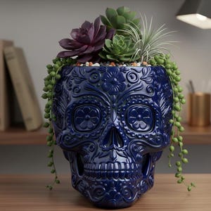 Pu&ograve; includere: Un vaso di ceramica blu scuro a forma di teschio con intricati disegni floreali. Il vaso &egrave; riempito con una variet&agrave; di piante grasse, tra cui una succulenta viola scuro, una succulenta verde e piante verdi pendenti. Il vaso &egrave; su una superficie di legno.
