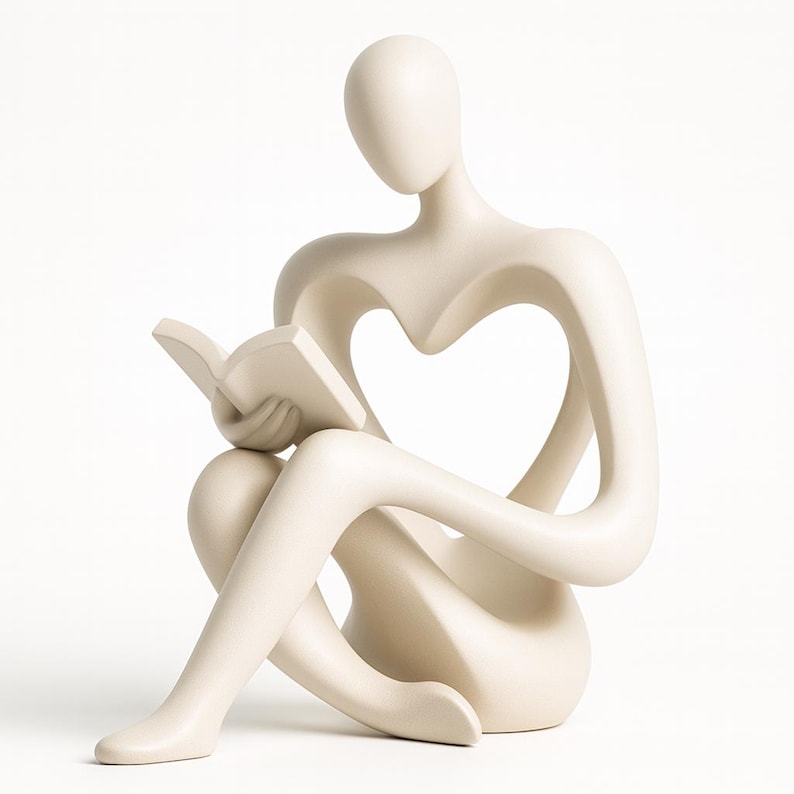 May include: A cream-colored sculpture of a person seated and reading a book. The figure has a heart-shaped cutout in the torso. The sculpture is smooth and minimalist, with a focus on form and negative space.